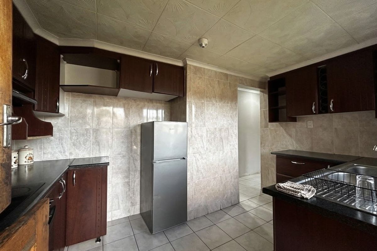 A functional kitchen featuring dark wood cabinetry, tiled walls, and tiled flooring, currently showing signs of wear and missing cabinet components.