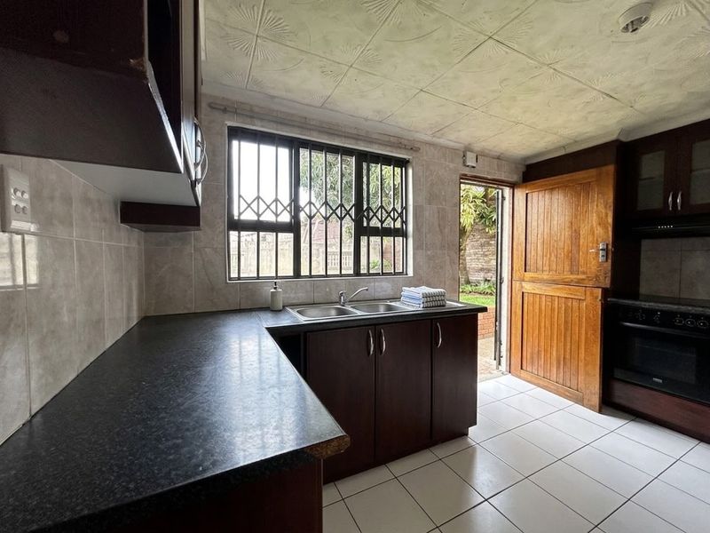 Functional kitchen featuring dark cabinetry, laminate countertops, double basin sink, tiled flooring, and direct access to the rear garden via a stable door.