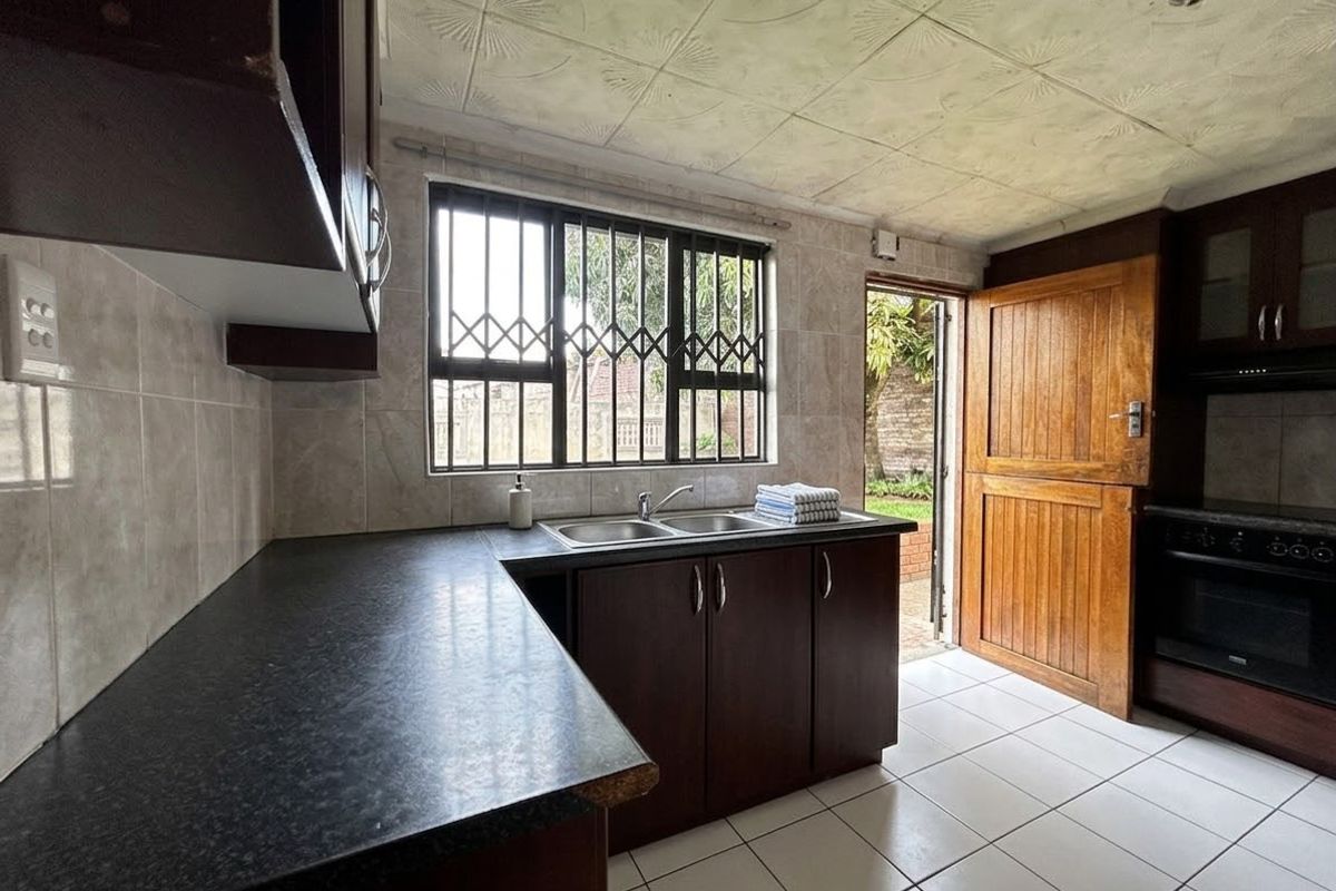 Functional kitchen featuring dark cabinetry, laminate countertops, double basin sink, tiled flooring, and direct access to the rear garden via a stable door.