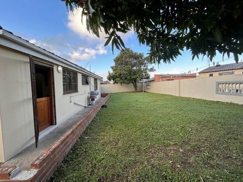 A rear garden area featuring a lawn, perimeter boundary walls, and a brick retaining wall along the side of the house.