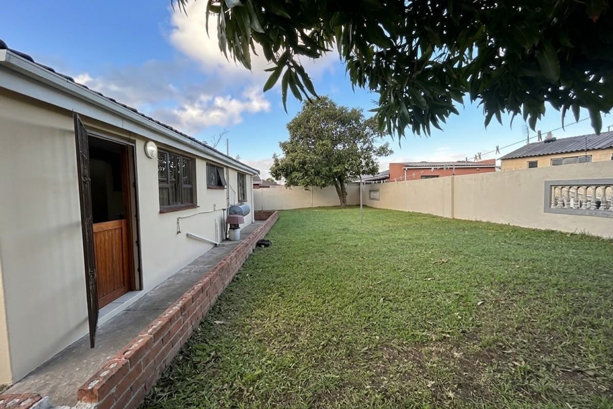 A rear garden area featuring a lawn, perimeter boundary walls, and a brick retaining wall along the side of the house.