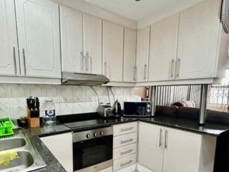 A functional kitchen featuring white cabinetry, granite countertops, a built-in oven, electric hob, and a tiled backsplash.