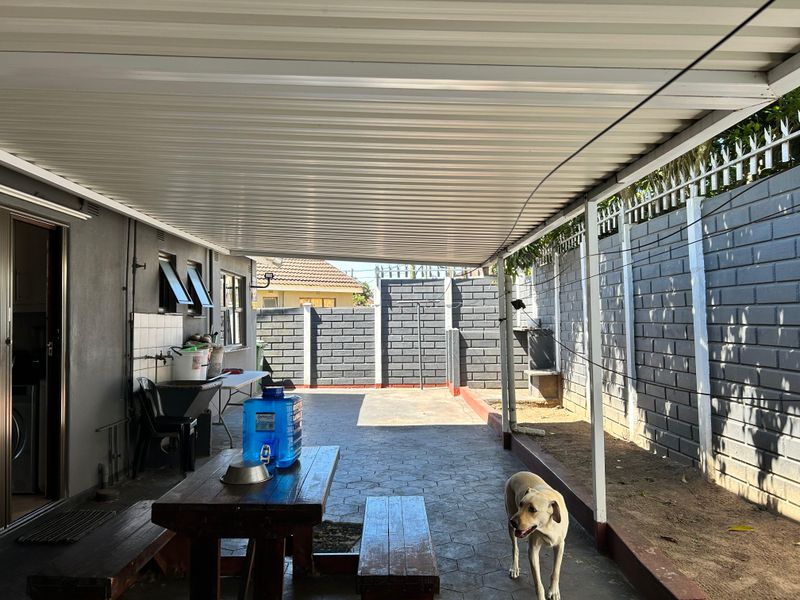 A covered outdoor patio area featuring paved flooring, a corrugated metal roof, and a secure perimeter wall with security spikes.