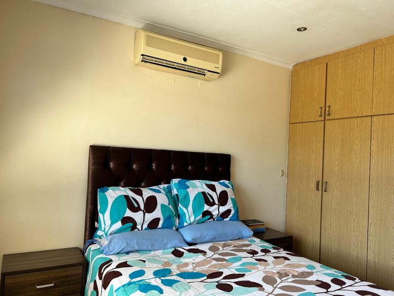 A bedroom featuring built-in wooden cupboards, a wall-mounted air conditioning unit, and recessed ceiling lighting.