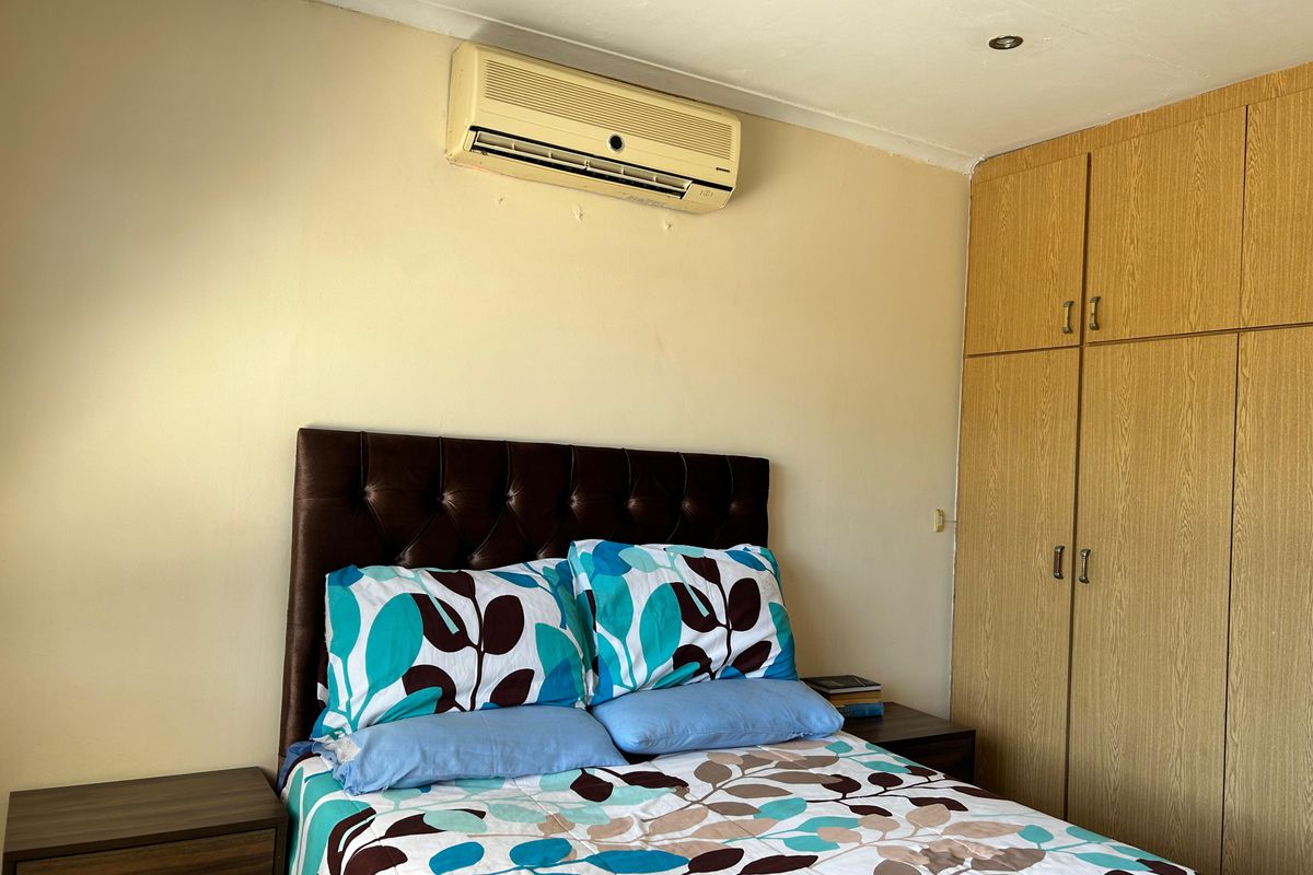 A bedroom featuring built-in wooden cupboards, a wall-mounted air conditioning unit, and recessed ceiling lighting.