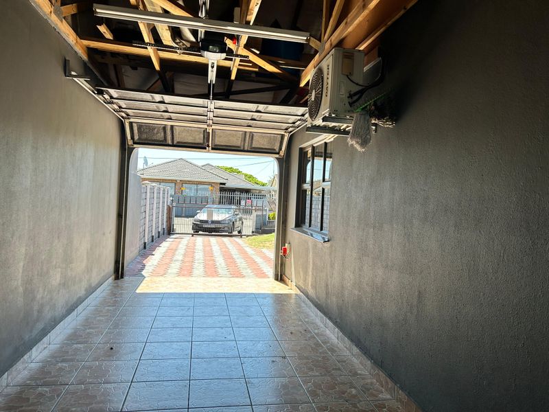 A functional garage space featuring tiled flooring, an automated sectional door, and an installed air conditioning unit, with exposed roof trusses.