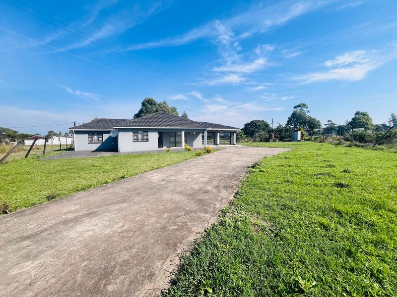 A single-story residential property featuring a tiled roof, security gates, and a long concrete driveway set on a spacious grassed lot.