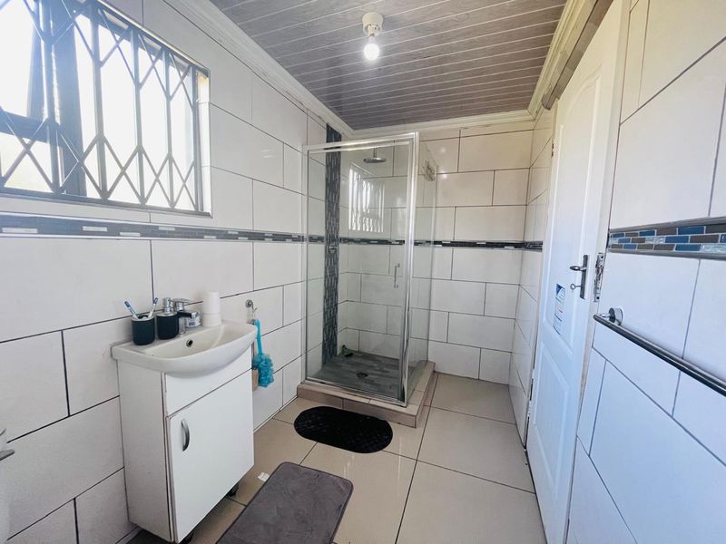 A functional bathroom featuring a glass shower enclosure, vanity basin, and tiled finishes throughout with security bars on the window.