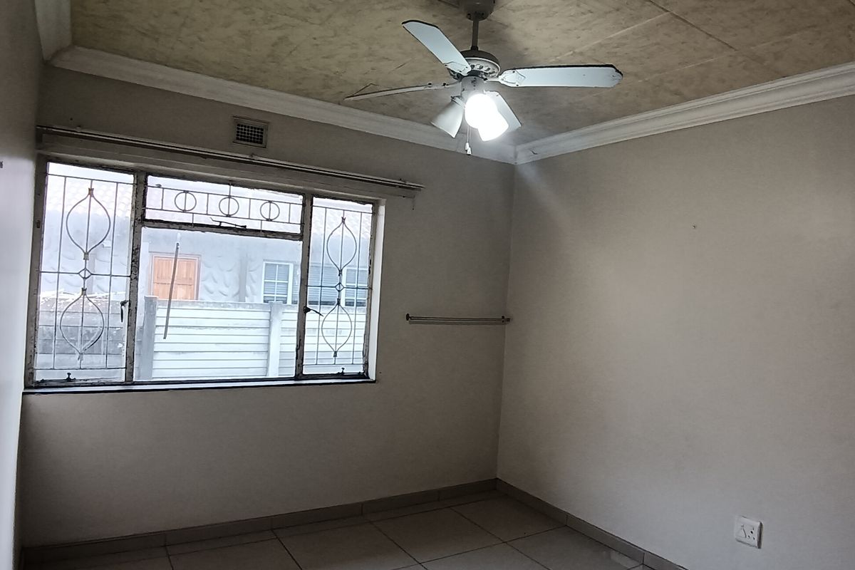 An empty bedroom featuring tiled flooring, a ceiling fan, and decorative ceiling tiles, with security bars installed on the window.