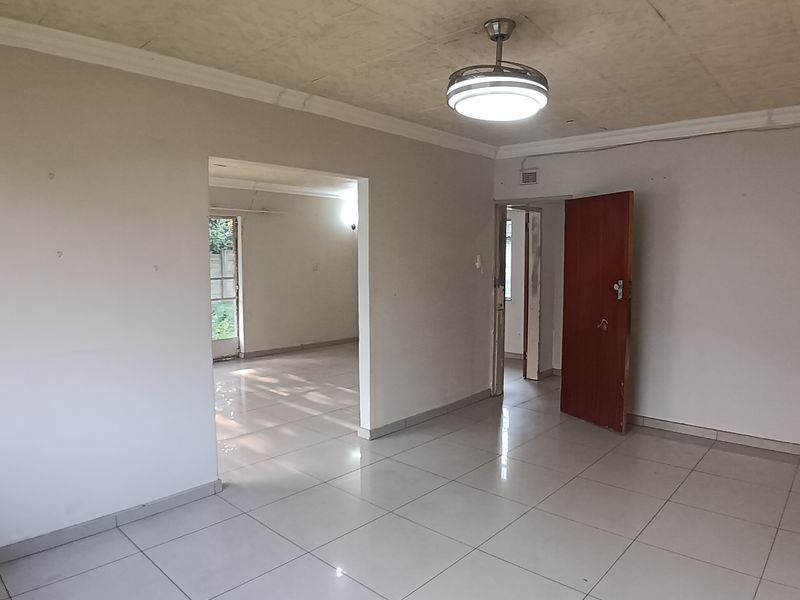 An empty living room featuring tiled flooring, a ceiling fan, and coved cornicing, leading into an adjacent room through an open doorway.