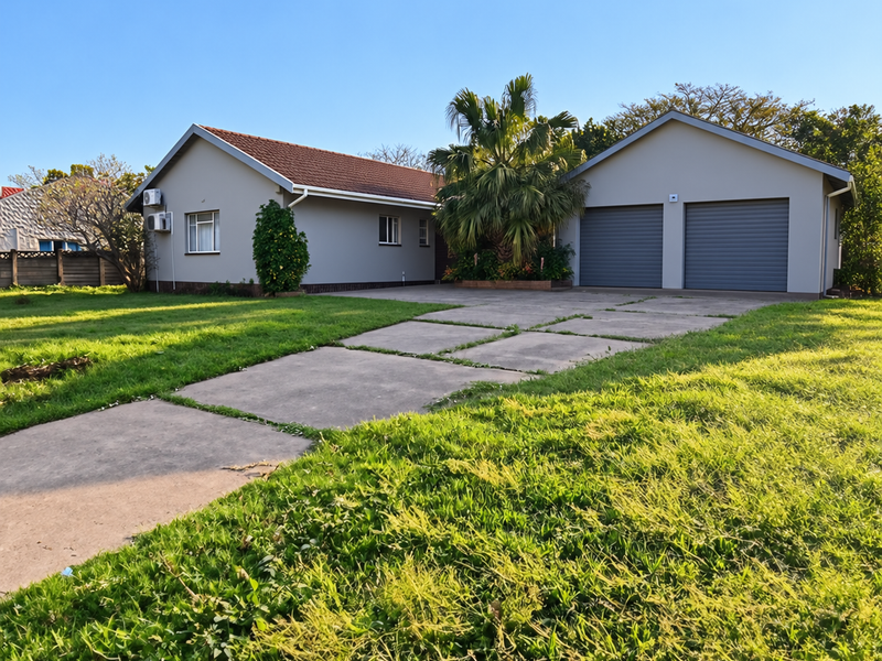 A well-maintained single-story house featuring a double garage, concrete driveway, and a spacious front lawn under a clear blue sky.