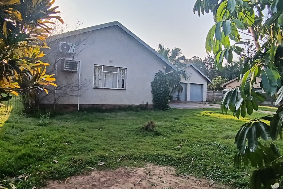 Rear view of the property featuring a lawn, double garage, and wall-mounted air conditioning unit.