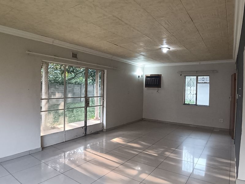 Spacious, empty living room featuring tiled flooring, a sliding glass door leading to the garden, and a wall-mounted air conditioning unit.