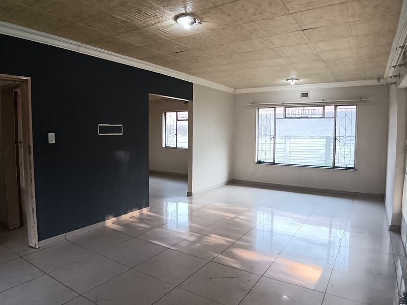 A spacious, empty living area featuring tiled flooring, decorative ceiling tiles, and large windows with security bars, offering a blank canvas for interior design.