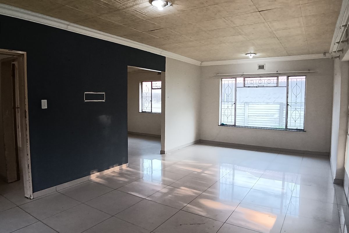 A spacious, empty living area featuring tiled flooring, decorative ceiling tiles, and large windows with security bars, offering a blank canvas for interior design.