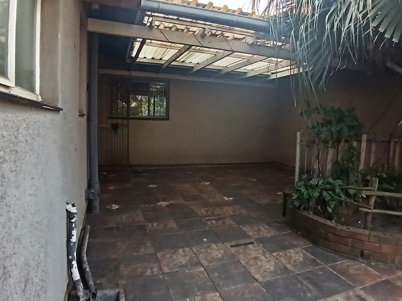 A covered outdoor patio area featuring tiled flooring, a translucent roof structure, and a built-in brick planter box.
