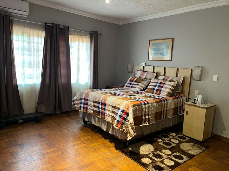 A spacious bedroom featuring warm parquet flooring, coved ceilings, and a wall-mounted air conditioning unit for climate control.
