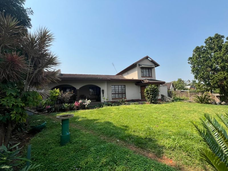 Rear view of a two-story house featuring an arched patio, lattice windows, and a spacious lawn area.