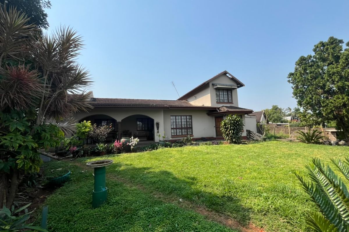 Rear view of a two-story house featuring an arched patio, lattice windows, and a spacious lawn area.