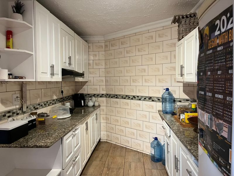 A functional kitchen featuring white cabinetry, granite countertops, a tiled backsplash, and wood-look floor tiles.