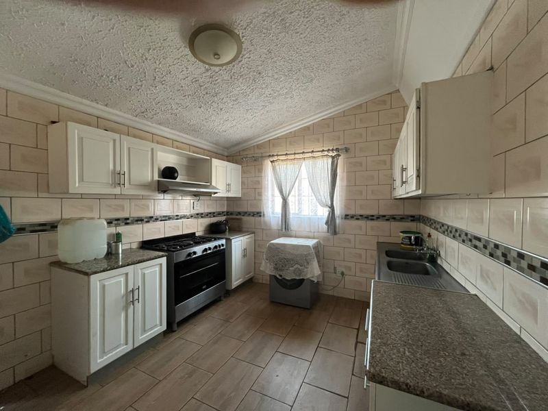 A functional kitchen featuring built-in cabinetry, granite countertops, a gas stove with extractor, and tiled finishes throughout.