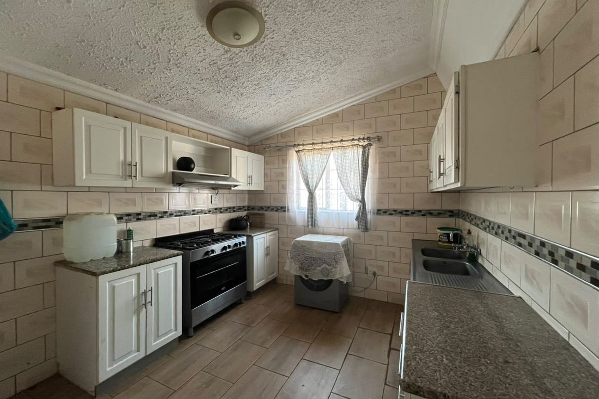 A functional kitchen featuring built-in cabinetry, granite countertops, a gas stove with extractor, and tiled finishes throughout.