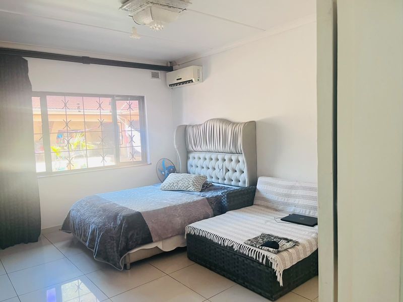 A bedroom featuring tiled flooring, an air conditioning unit, and a window with security bars, offering a functional and well-lit living space.