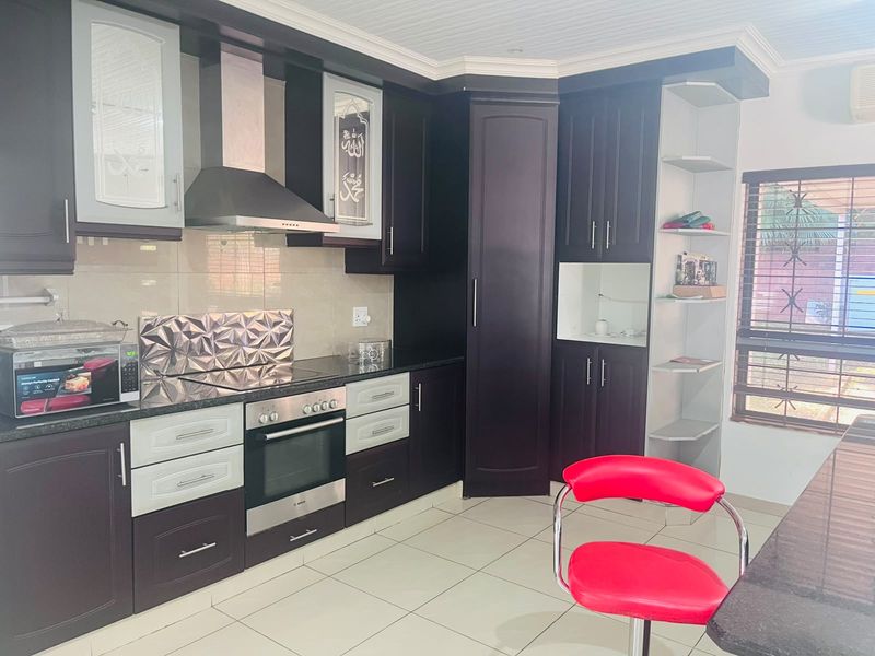 Modern kitchen featuring dark wood cabinetry, granite countertops, built-in oven, extractor fan, and tiled flooring with natural light from the window.