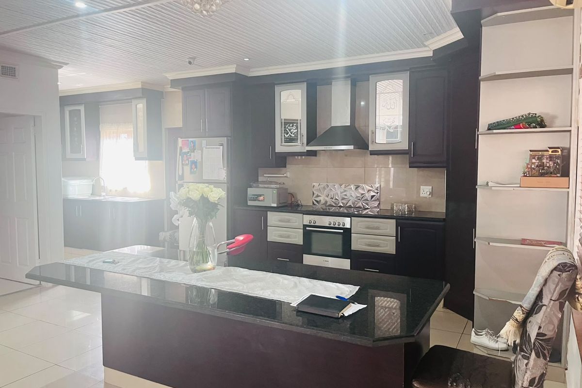 Spacious kitchen featuring dark cabinetry, a large granite-topped island, built-in oven, extractor fan, and tiled flooring with a secondary scullery area visible.