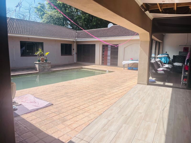Outdoor pool area featuring a tiled patio, covered entertainment space, and direct access to the home via sliding doors.