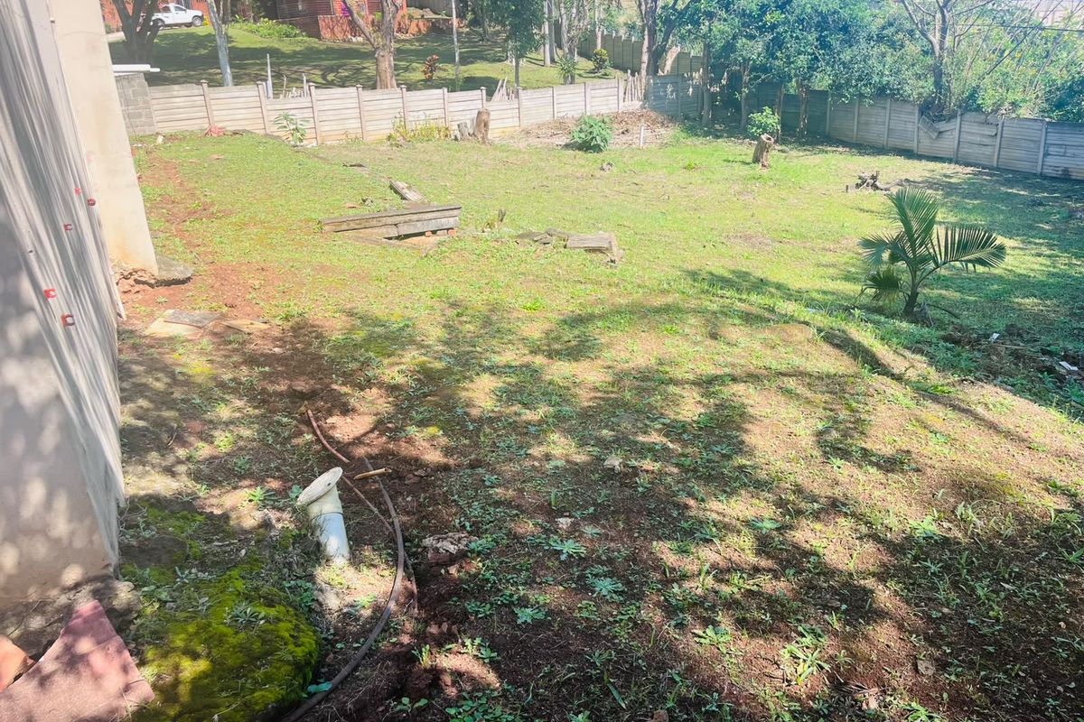 A spacious rear garden area featuring a precast concrete boundary wall and uneven terrain, offering significant potential for landscaping and outdoor development.