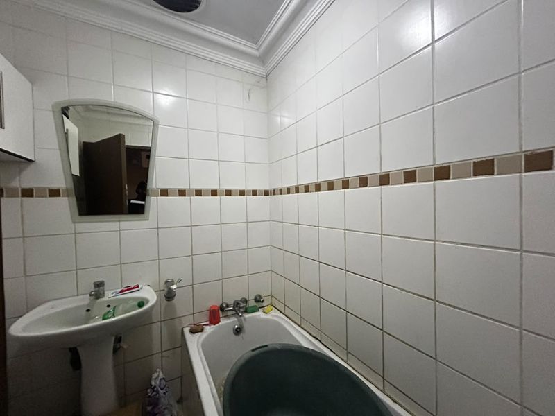 A compact bathroom featuring a pedestal basin, bathtub, and full-height wall tiling with a decorative accent border.