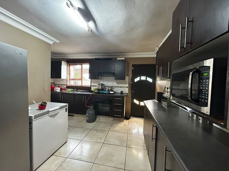A functional kitchen featuring dark cabinetry, laminate countertops, built-in oven, extractor fan, and tiled flooring with direct access to an exterior door.