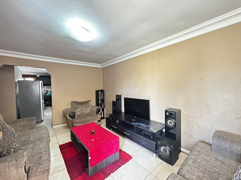 A living room featuring tiled flooring and ceiling cornicing, currently showing signs of wall surface wear and requiring cosmetic updates.