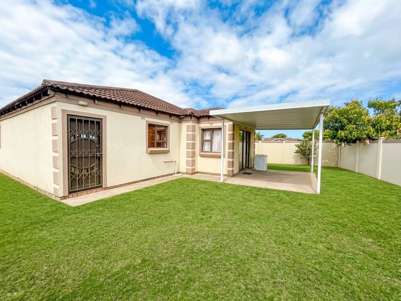 Rear view of the house featuring a well-maintained lawn, a covered patio area, and secure access points with perimeter walling.