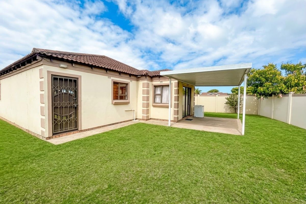 Rear view of the house featuring a well-maintained lawn, a covered patio area, and secure access points with perimeter walling.
