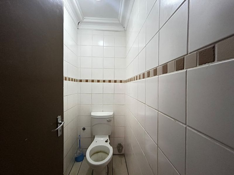 A compact guest bathroom featuring full-height ceramic wall tiles, crown molding, and a standard toilet fixture.
