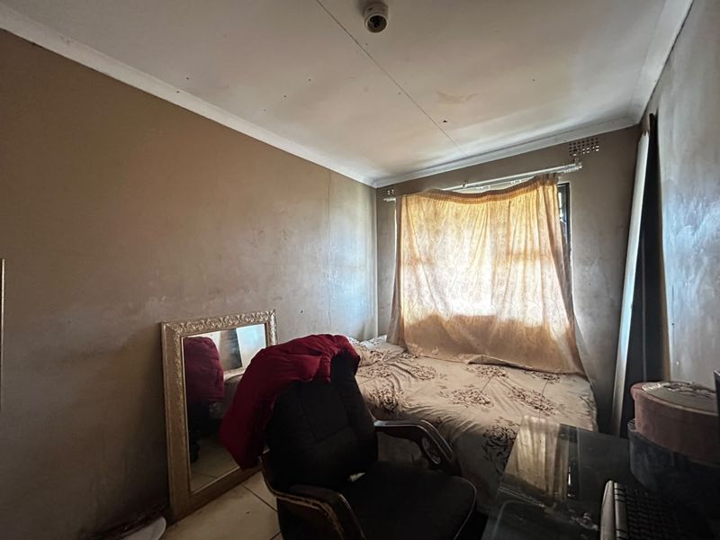 A bedroom featuring plain walls and a window with security bars, currently requiring cosmetic updates and maintenance to improve its overall condition.