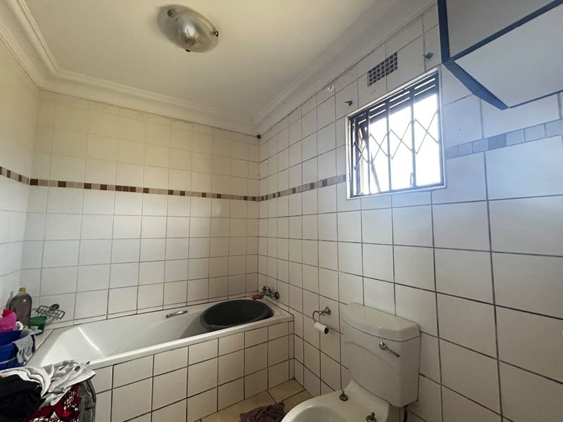 A dated bathroom featuring a built-in bathtub, ceramic wall tiling, and a standard toilet, requiring cosmetic updates to modernize the space.