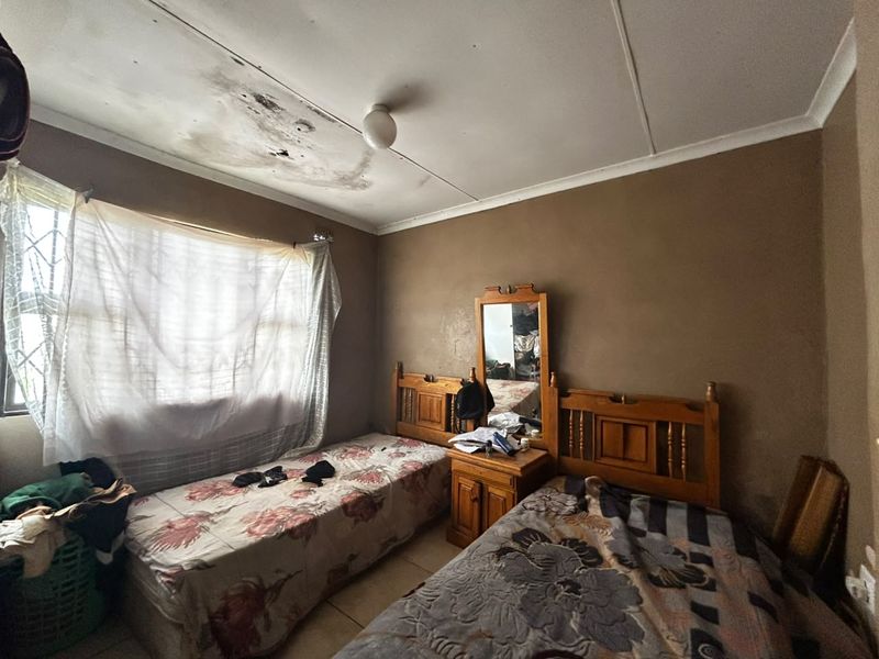 A bedroom featuring tiled flooring and security bars on the window, currently showing significant ceiling water damage and signs of wear.
