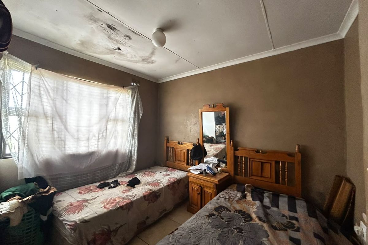 A bedroom featuring tiled flooring and security bars on the window, currently showing significant ceiling water damage and signs of wear.