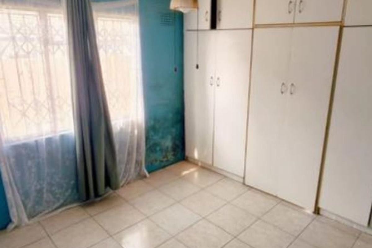 A bedroom featuring built-in cupboards, tiled flooring, and a ceiling fan. The room shows signs of wall damp and requires maintenance.