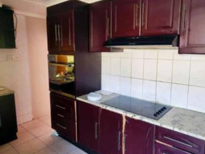 A dated kitchen featuring dark wood-finish cabinetry, built-in oven, ceramic hob, and tiled backsplash, requiring cosmetic updates to improve its aesthetic appeal.