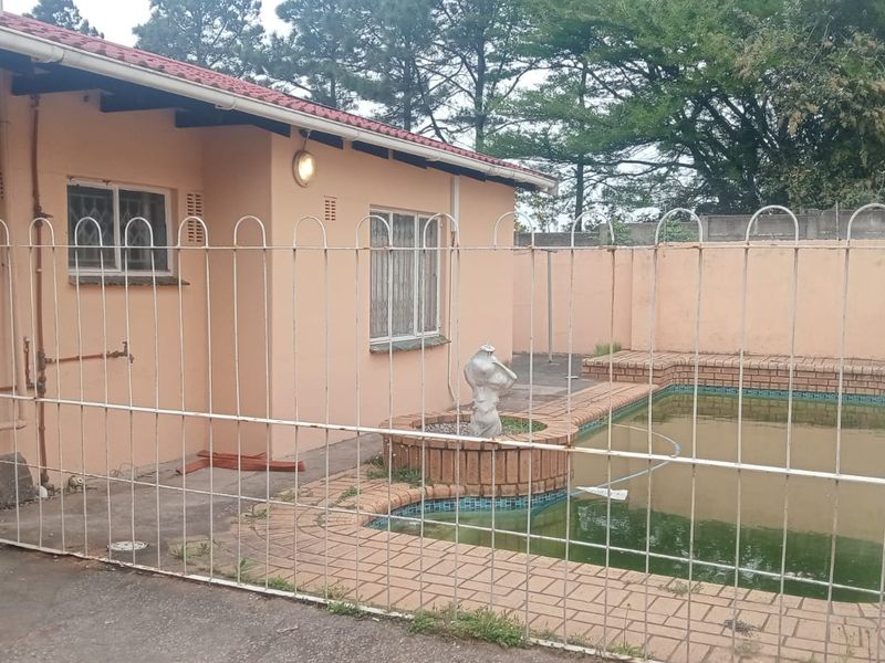 Rear exterior view featuring a swimming pool with brick surround, enclosed by metal security fencing and a perimeter boundary wall.