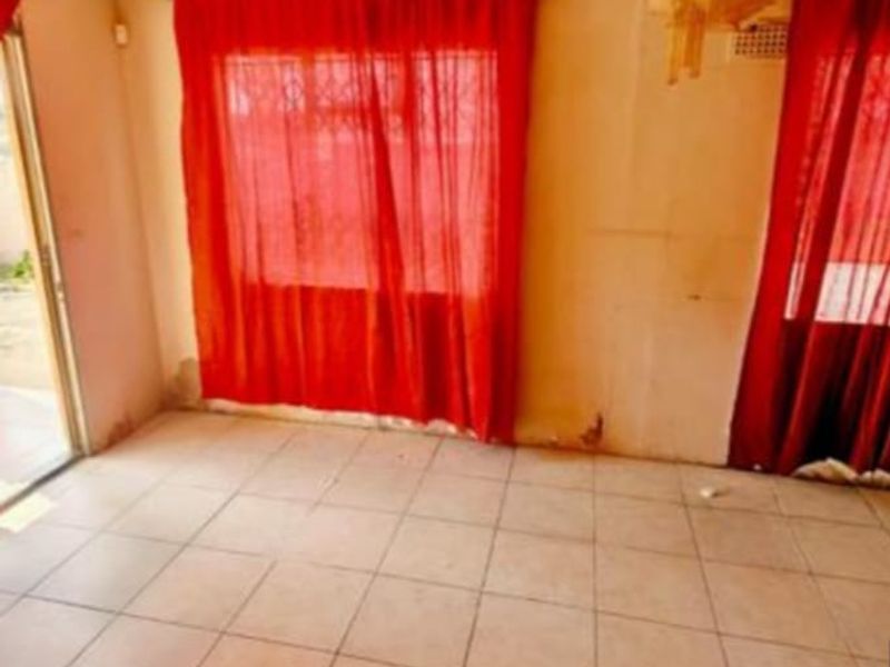 An empty living room featuring tiled flooring and a sliding glass door, requiring cosmetic updates to the wall finishes.