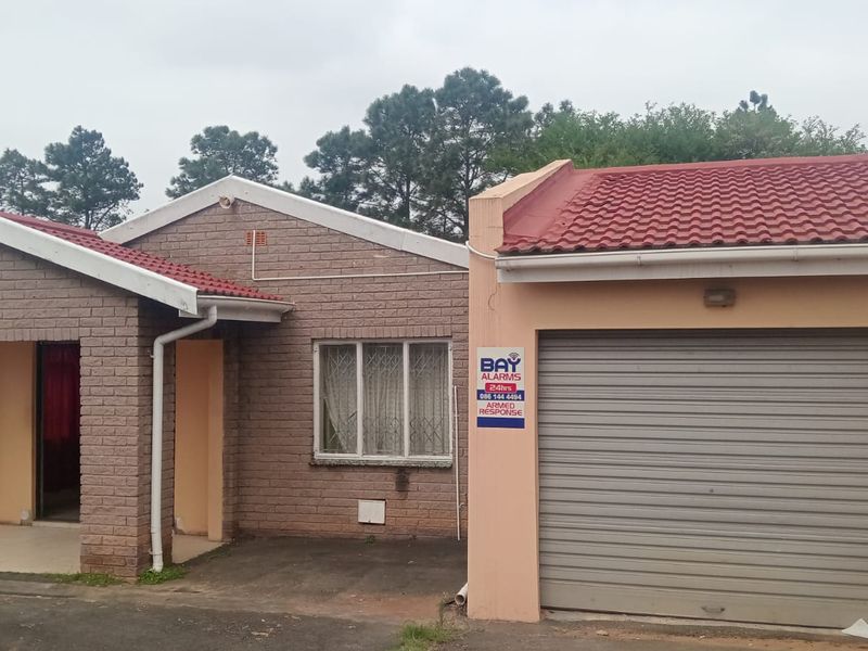 Front elevation of a single-story brick house featuring a tiled roof, integrated garage with a roller shutter door, and a covered entrance porch.