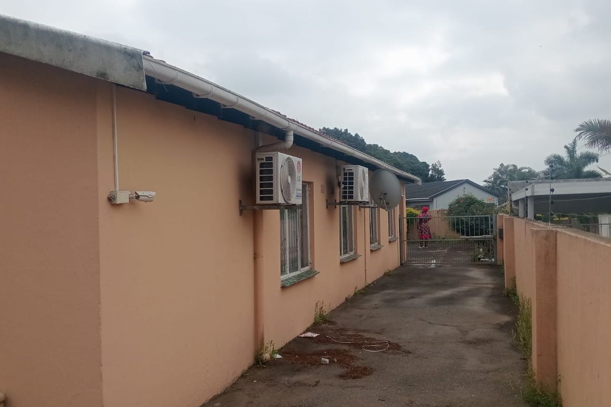 Side exterior view of the property featuring a concrete driveway, boundary wall, and mounted air conditioning units.