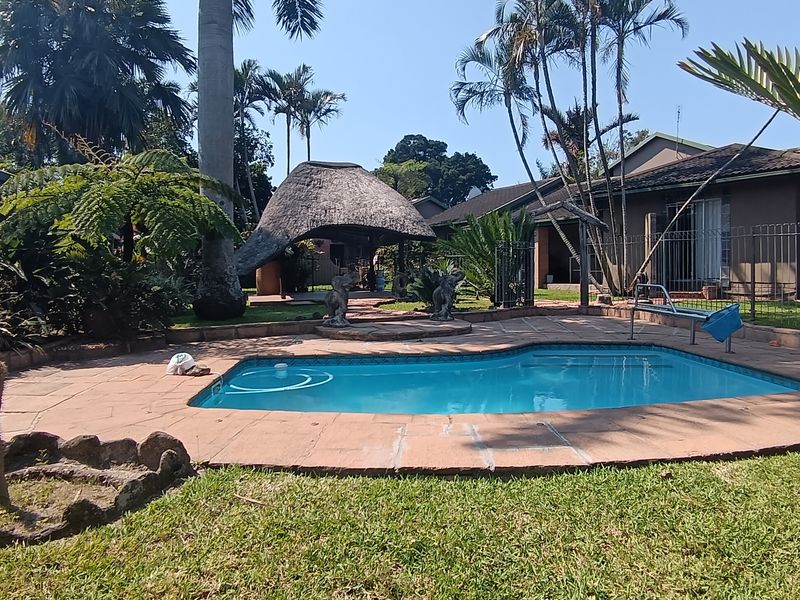 Outdoor pool area featuring a swimming pool, paved surround, and a thatched lapa set within a landscaped garden.