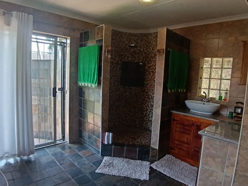 A bathroom featuring a walk-in tiled shower, a vessel sink on a wooden vanity with granite countertop, and access to an outdoor area.