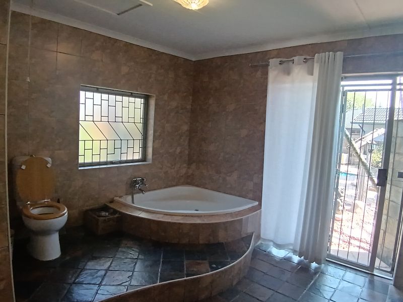 A spacious bathroom featuring a corner bathtub, tiled walls and flooring, and direct access to the outdoor area through a sliding door.